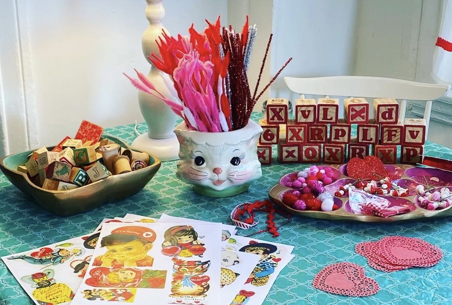 A table filled with various piles of craft supplies for a Valentines day themed craft.